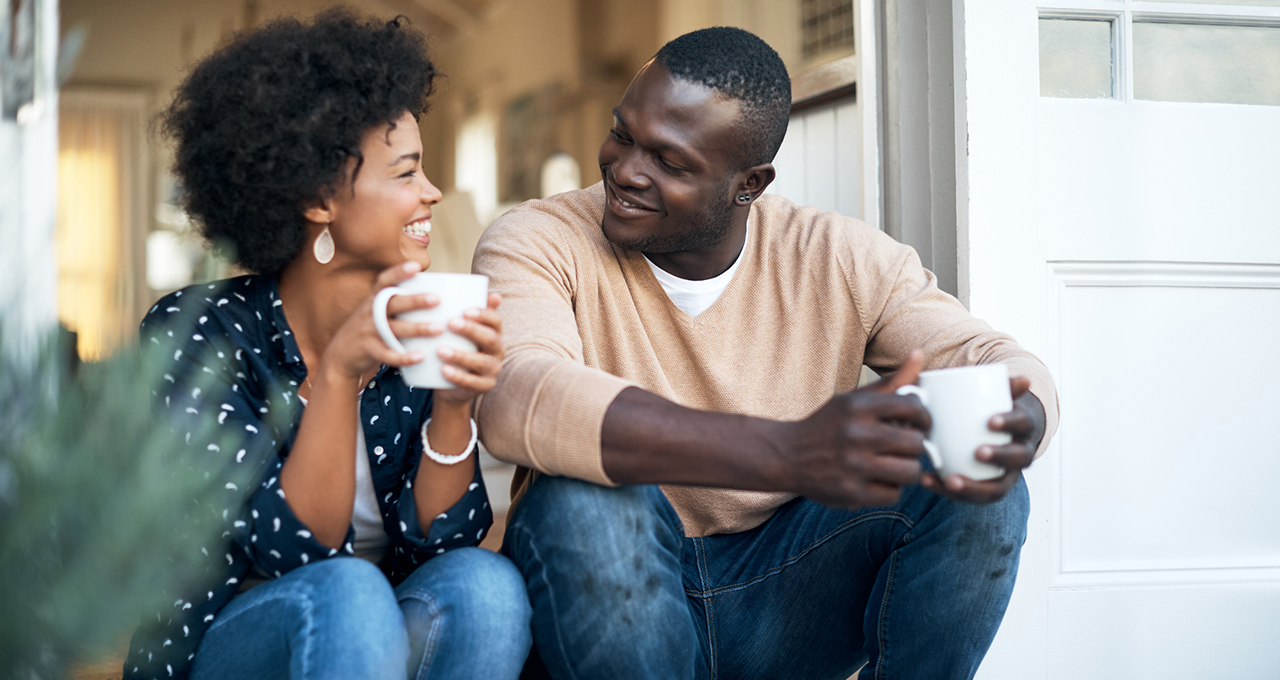 Black couple holding cups of coffee looking at each other smiling