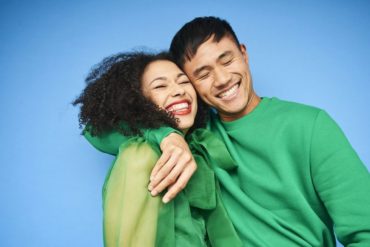 Interracial couple wearing green sweatshirts smiling and laughing with one another